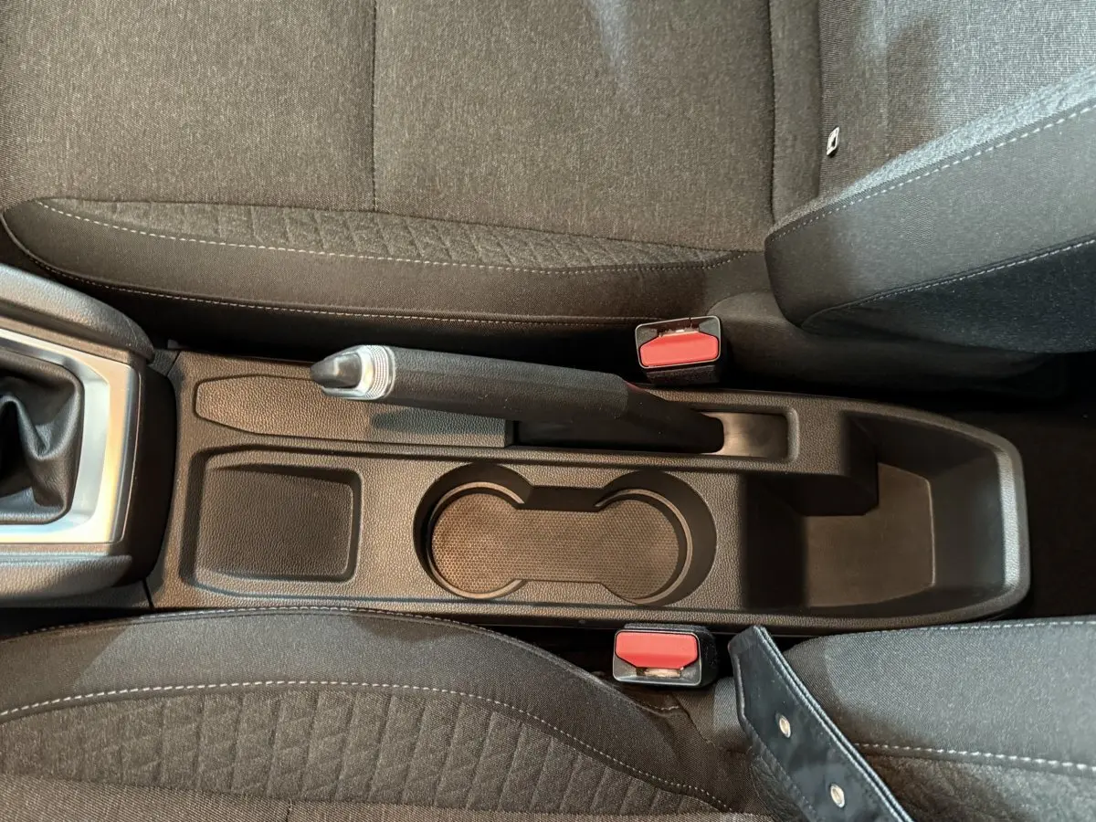 Vue plongeante sur la console centrale noire de la Renault Clio Business blanche, avec frein à main manuel et porte-gobelets.