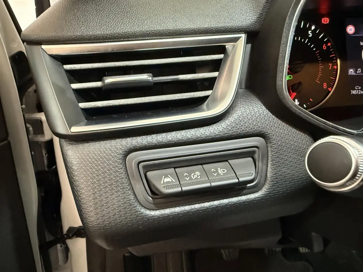 Gros plan sur les commandes d’assistance et réglage des phares à gauche du tableau de bord d’une Renault Clio Business blanche.