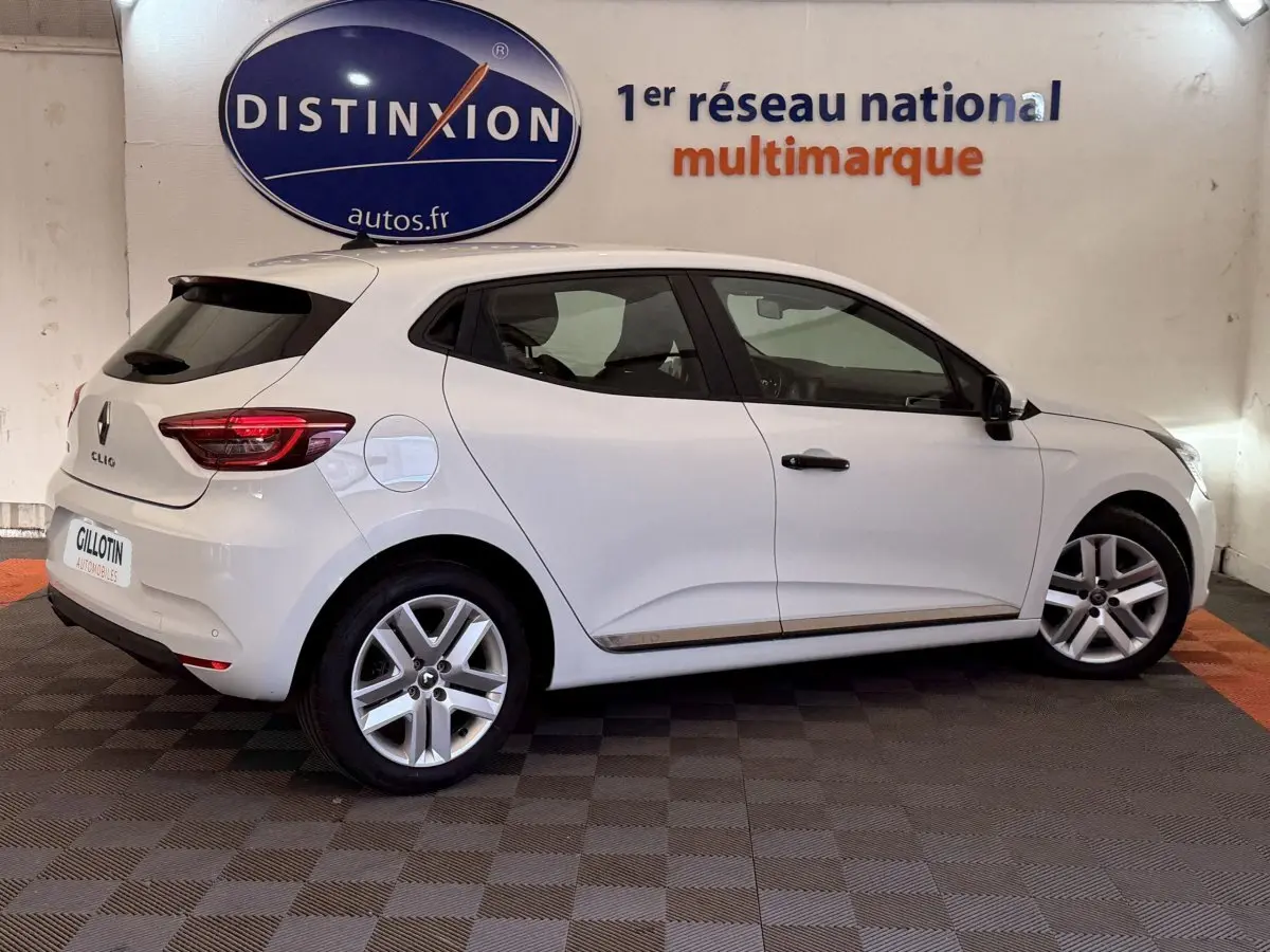 Profil droit d'une Renault Clio Business blanche de 2021, avec jantes alliage et feux arrière LED visibles en intérieur showroom.