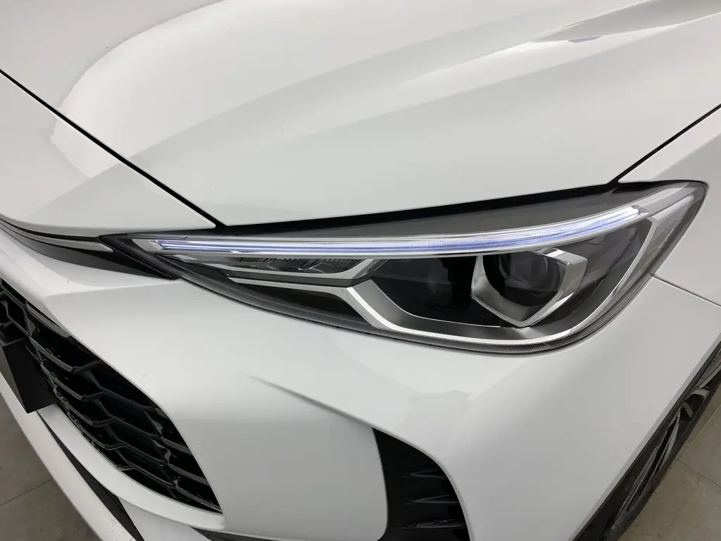 Gros plan sur le phare avant droit blanc Dover White du MG ZS 1.5 L Hybrid+ 197 ch Luxury avec calandre noire ajourée.