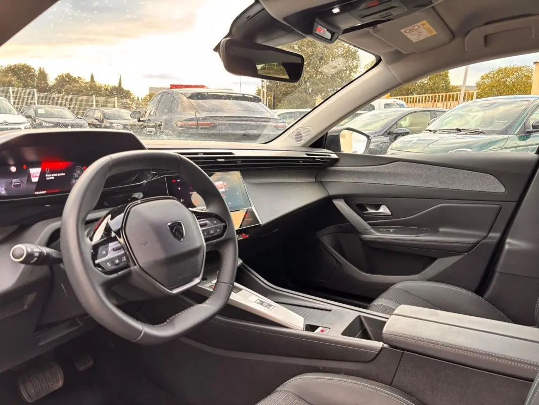 Intérieur de la Peugeot 308 Hybrid 145 gris, vue côté conducteur montrant le volant compact et le cockpit numérique.