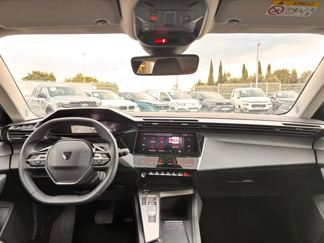Vue intérieure frontale du cockpit numérique gris de la Peugeot 308 Hybrid 145 e-DCS6 Allure avec volant compact et écran tactile central.