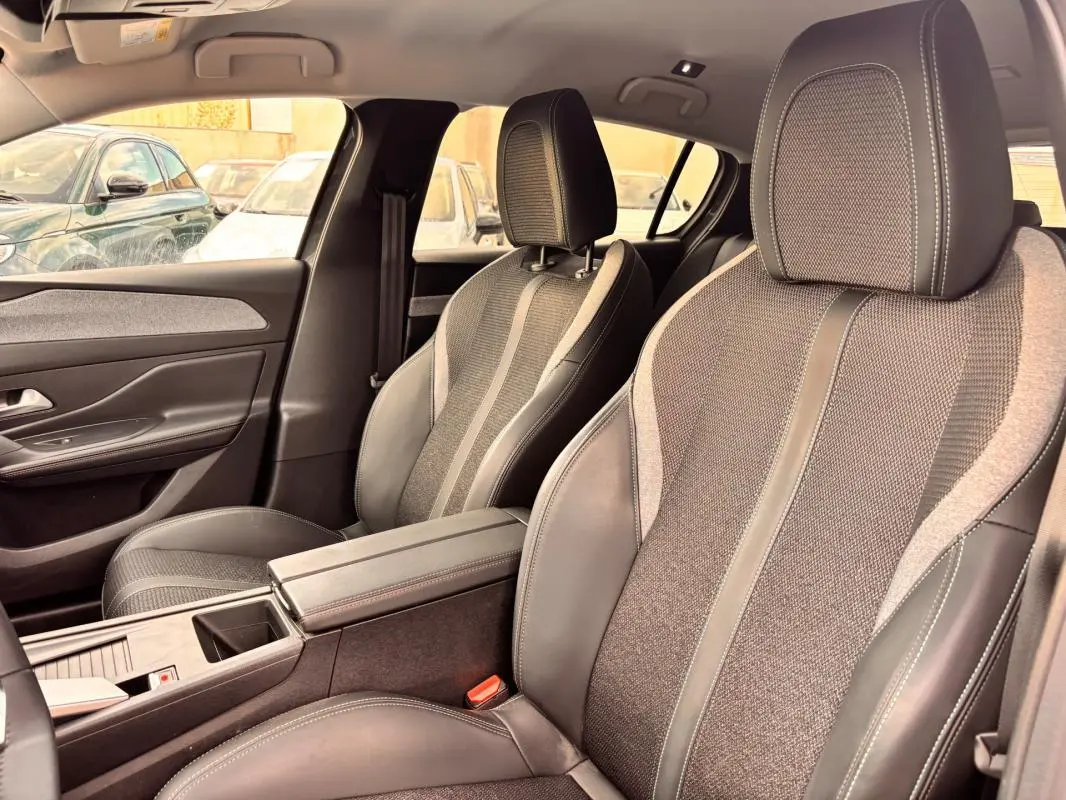 Vue intérieure côté avant droit du Peugeot 308 Hybrid 145 gris, avec sièges tissu et cuir, accoudoir central et port USB.