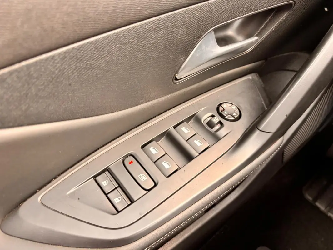Vue rapprochée de la porte côté conducteur d'une Peugeot 308 gris, montrant les commandes électriques des vitres et des rétroviseurs.