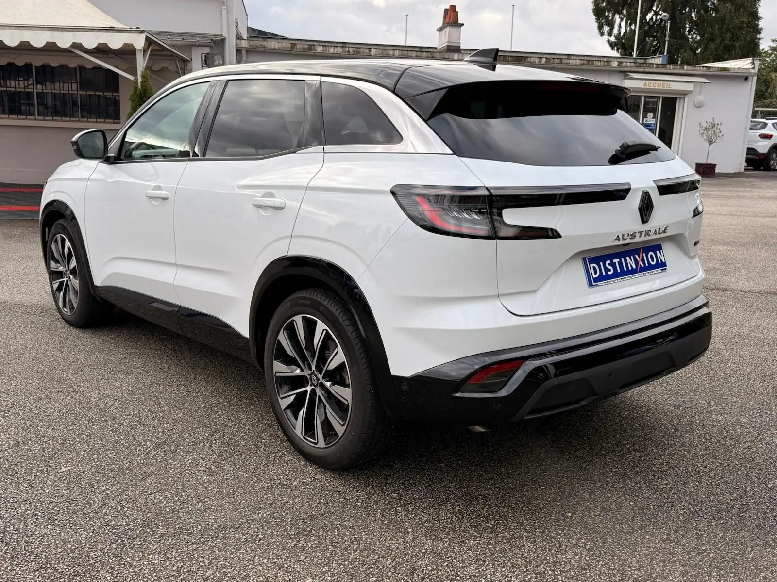 Vue arrière côté gauche du Renault Austral blanc nacré avec toit noir et jantes alliage, stationné sur un parking extérieur.