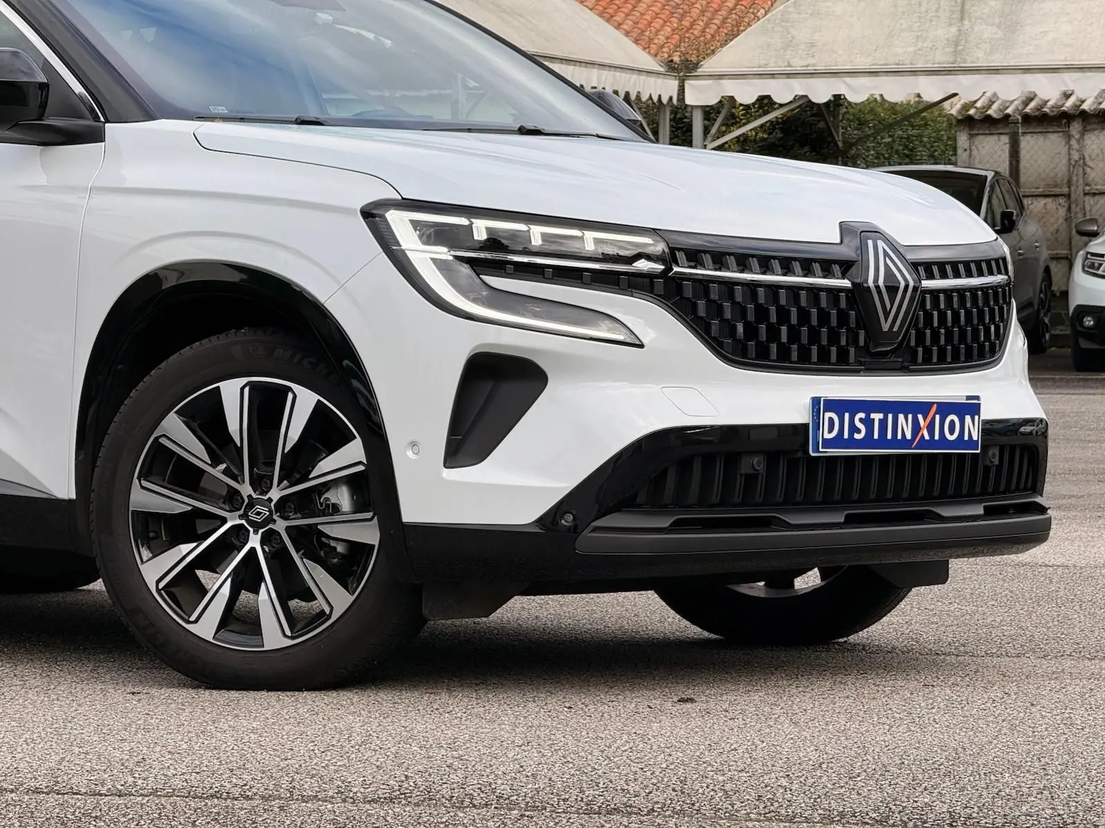 Vue 3/4 avant gauche du Renault Austral E-Tech blanc nacré avec toit noir, mettant en valeur sa calandre et ses jantes bicolores.