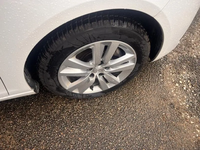 Gros plan sur la roue avant droite avec jante alu de la Peugeot 308 blanc banquise sous la pluie.