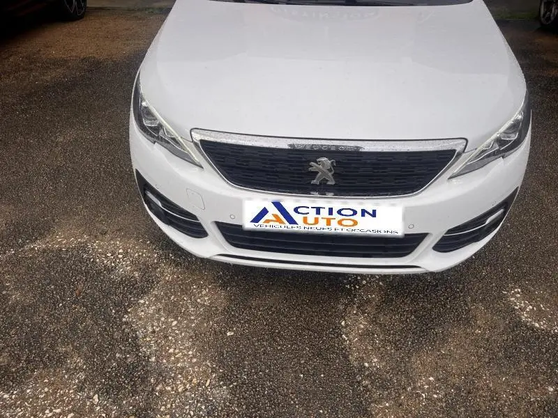 Vue avant rapprochée d’une Peugeot 308 blanche Banquise avec calandre noire et logo lion central visible.