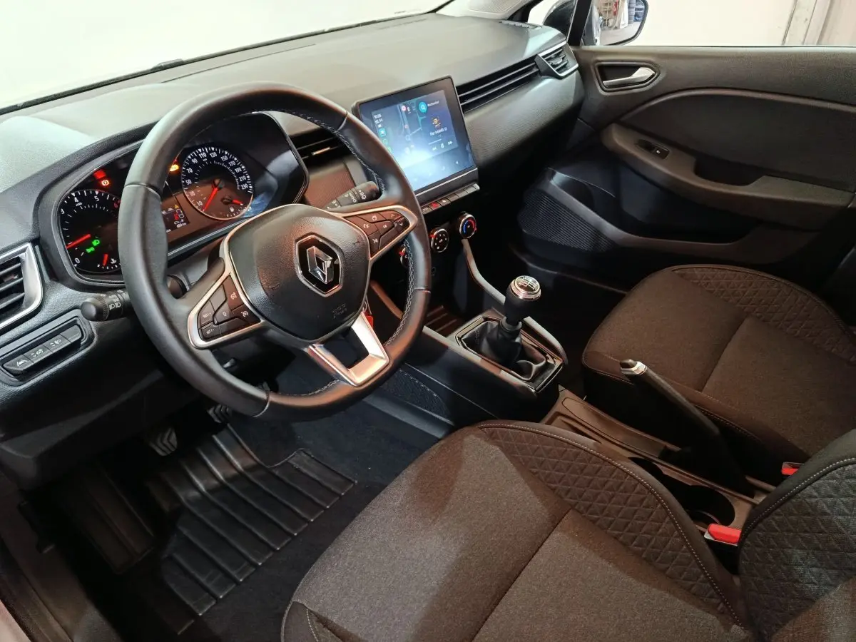 Vue intérieure côté conducteur de la Renault Clio gris clair 2023, volant cuir multifonctions et écran tactile central.