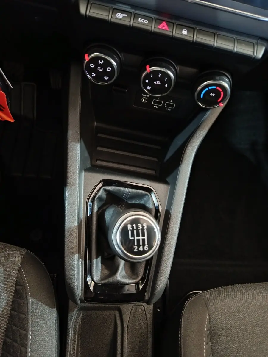 Vue plongeante sur la console centrale de la Renault Clio gris clair 2023, mettant en valeur le levier de vitesses manuel et les commandes de climatisation.