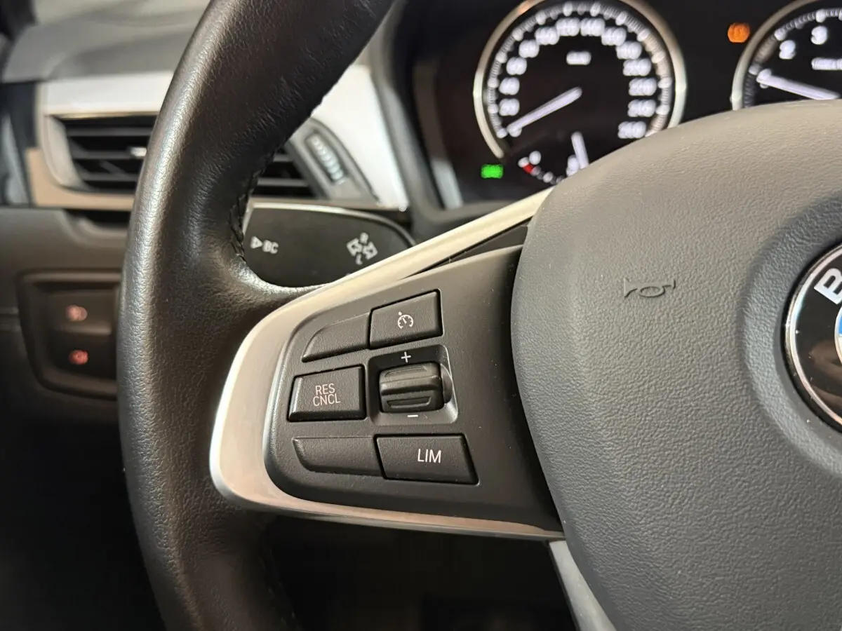 Gros plan sur le volant cuir et alu de la BMW X2 sDrive18i 2023, avec commandes multifonctions côté gauche.