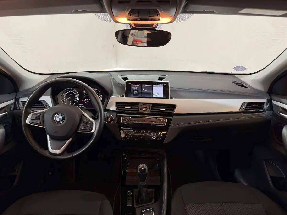 Vue frontale de l'intérieur du BMW X2 sDrive18i Lounge 2023, tableau de bord noir avec écran central et volant cuir.
