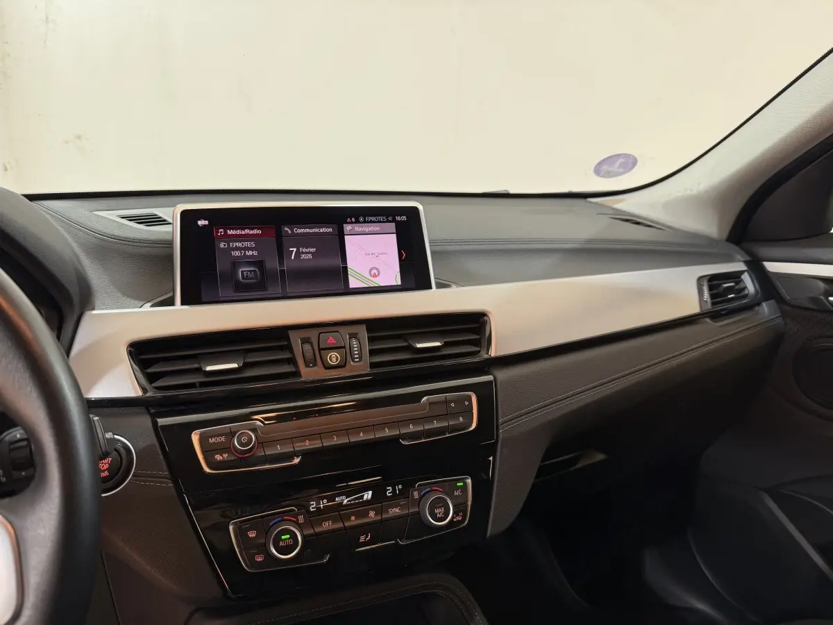 Vue intérieure du tableau de bord de la BMW X2 sDrive18i Lounge 2023 avec écran central et commandes climatisation.