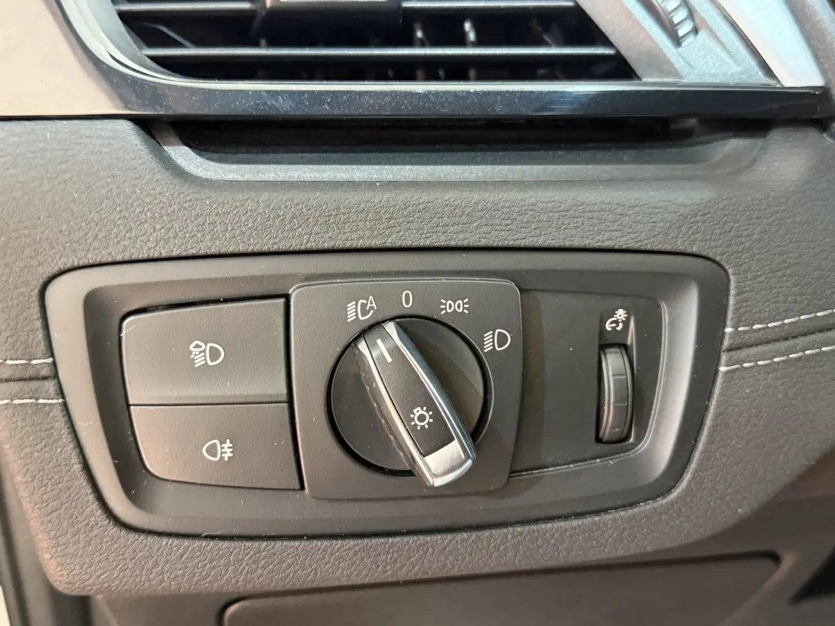 Gros plan sur le bouton de commande des phares de la BMW X2 sDrive18i Lounge 2023, entouré de plastique noir texturé.