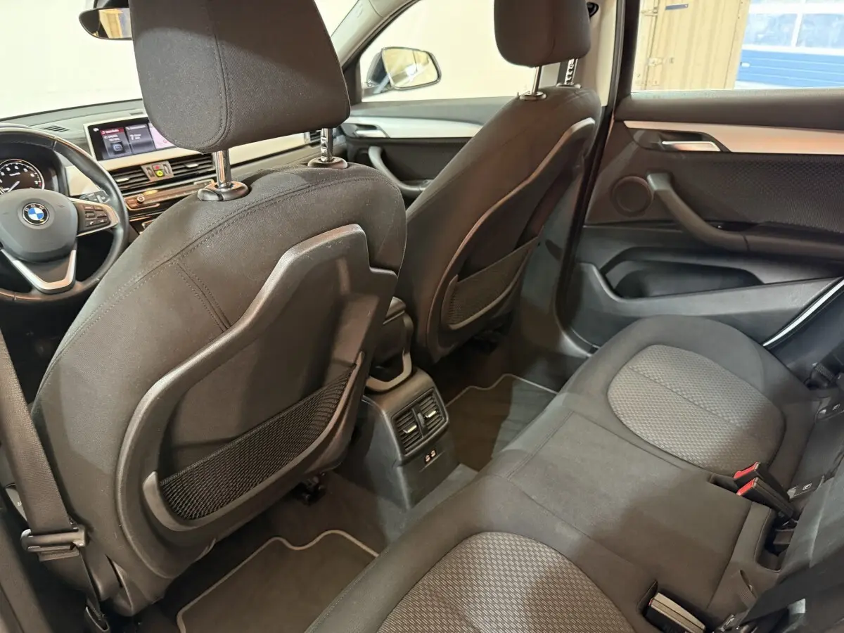 Vue intérieure arrière côté droit de la BMW X2 sDrive18i Lounge 2023 avec sièges tissu noirs et console centrale.
