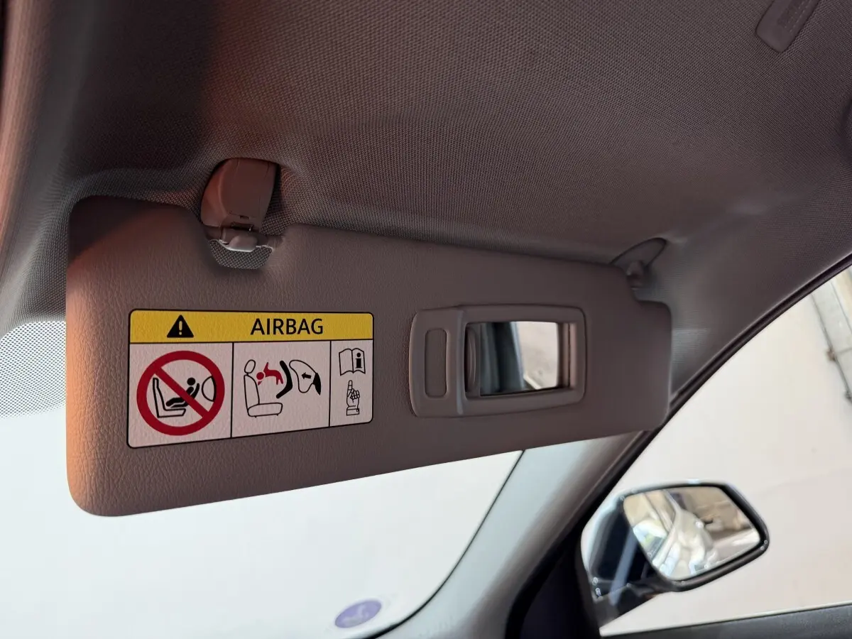 Détail du pare-soleil gris avec miroir intégré et avertissement airbag, côté gauche intérieur d'une BMW X2 blanc.