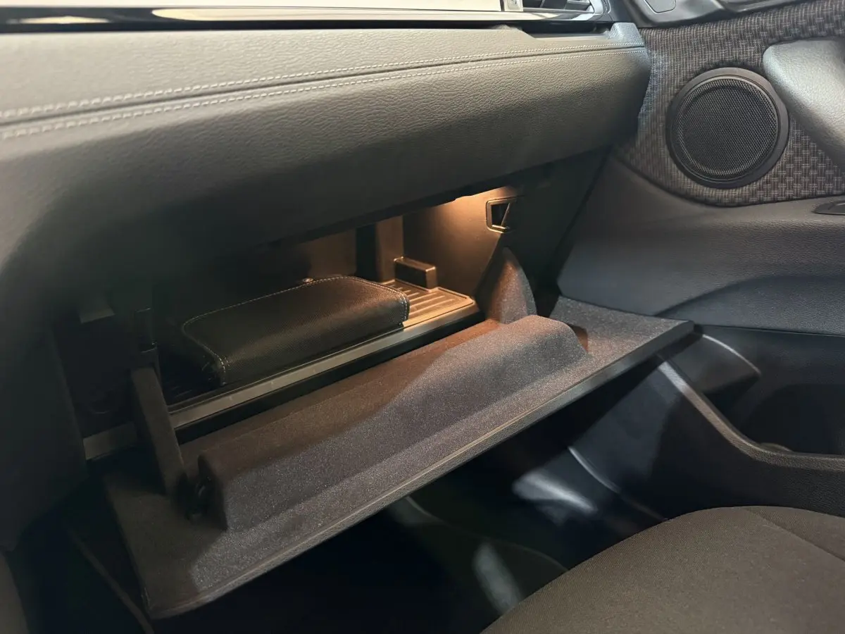 Vue intérieure du vide-poche passager ouvert d'une BMW X2 sDrive18i Lounge 2023, avec éclairage intérieur doux.