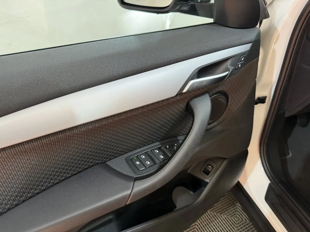 Vue rapprochée de la porte avant gauche blanche du BMW X2 sDrive18i Lounge, avec commandes des vitres et poignée noire.
