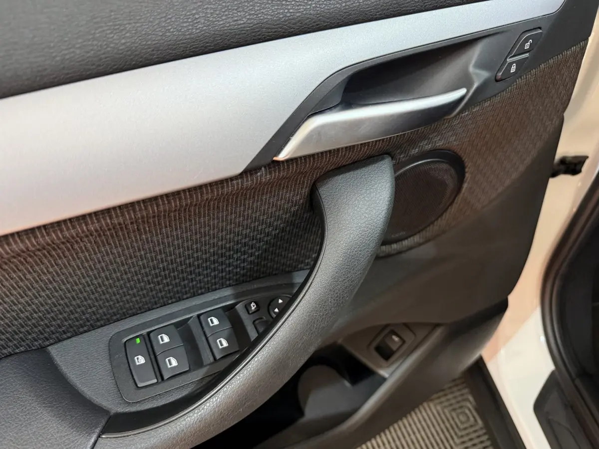 Gros plan sur la porte avant gauche blanche d'une BMW X2 2023, avec commandes de vitres et poignée intérieure noire.