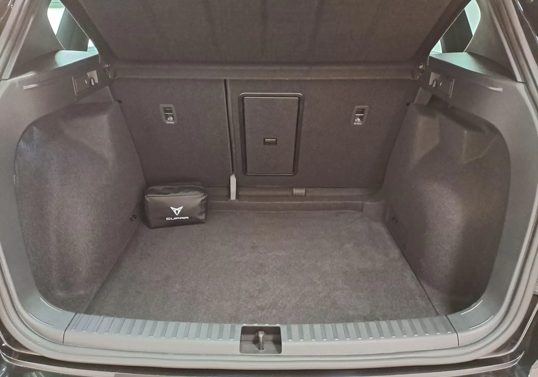 Coffre ouvert du CUPRA Ateca 2024 noir magique, vue arrière montrant un espace de rangement avec trousse de secours CUPRA.