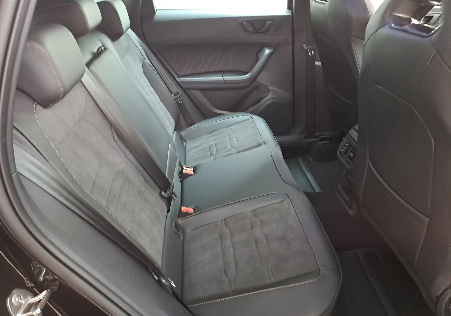 Vue intérieure des sièges arrière noirs avec surpiqûres orange du CUPRA Ateca 2024, version 1.5 TSI essence, côté gauche.