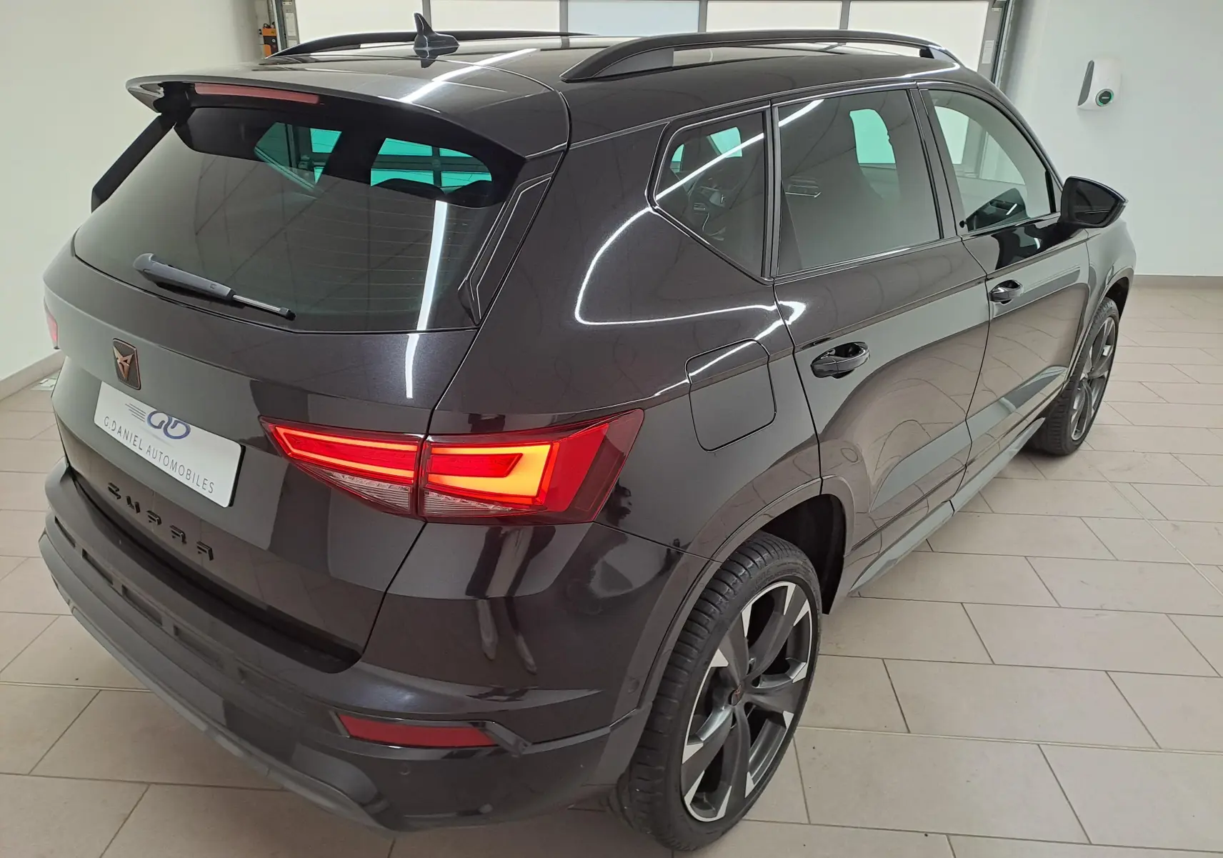 Vue 3/4 arrière droite du CUPRA Ateca 1.5 TSI 150 DSG7 2024 en noir magique avec feux arrière allumés et jantes sport.