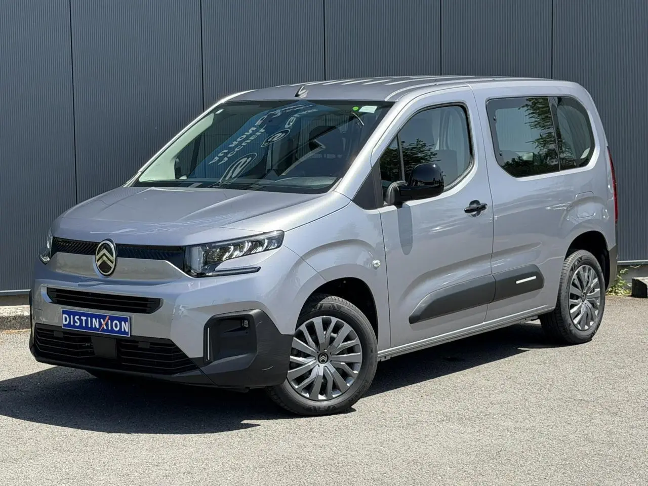 Vue 3/4 avant droit du Citroën Berlingo ë-136 gris Artense avec jantes tôles et protections latérales noires.