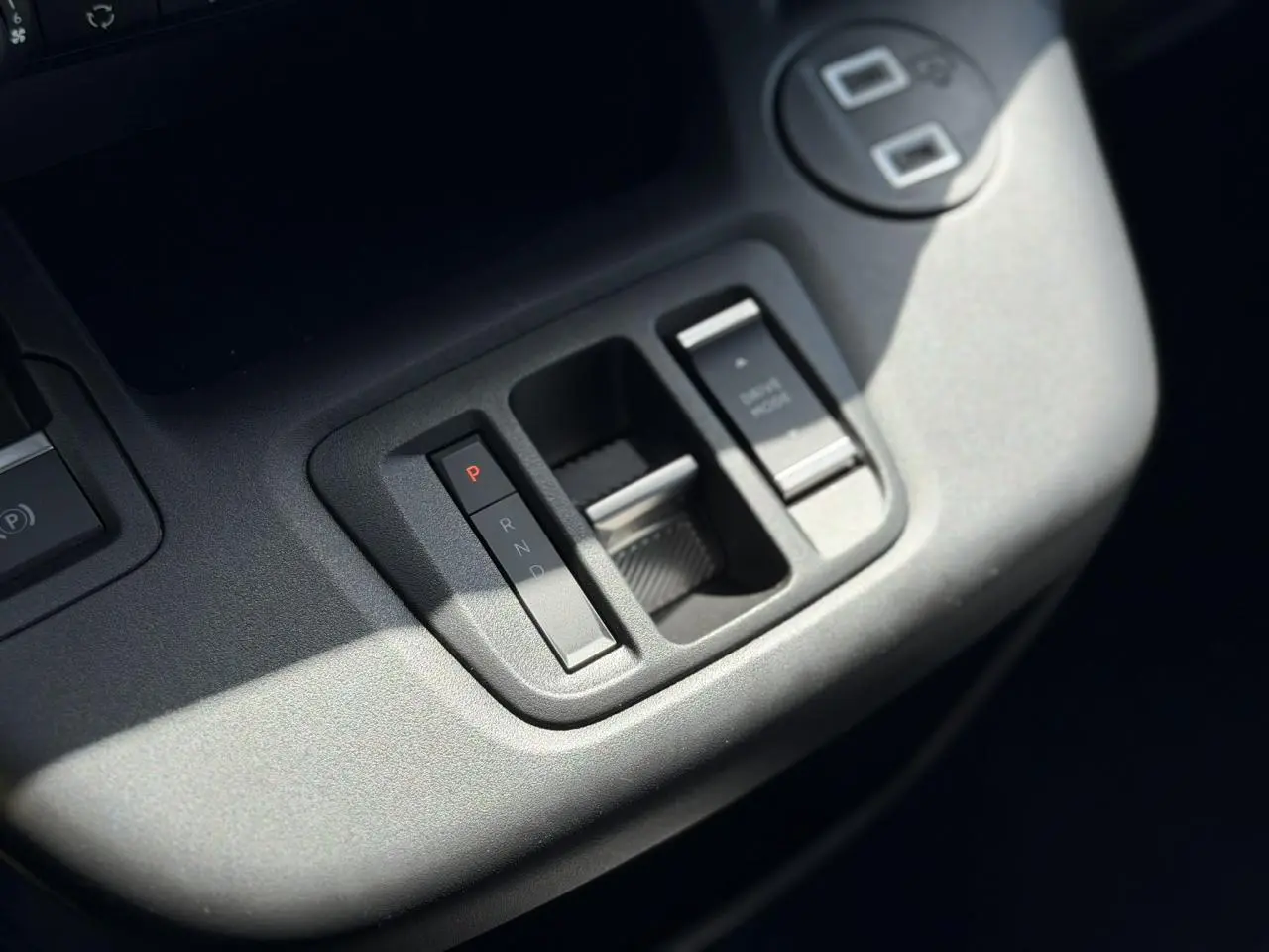 Gros plan sur la console centrale grise du Citroën Berlingo ë-136, montrant la commande de boîte automatique et frein de stationnement.