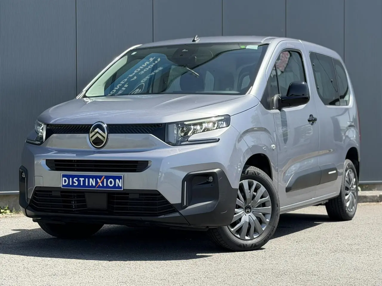 Vue 3/4 avant du Citroën Berlingo ë-136 gris Artense avec jantes tôles et pare-chocs noirs contrastés.