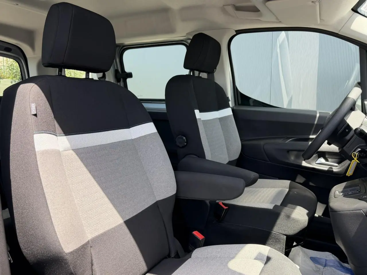 Vue intérieure côté conducteur du Citroën Berlingo ë-136 2025, sièges tissu bicolore gris et noir avec accoudoirs.