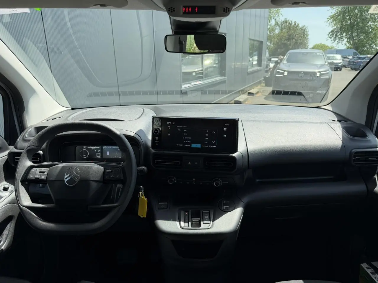 Vue intérieure du tableau de bord du Citroën Berlingo ë-136 gris Artense, avec écran tactile central et volant multifonction.