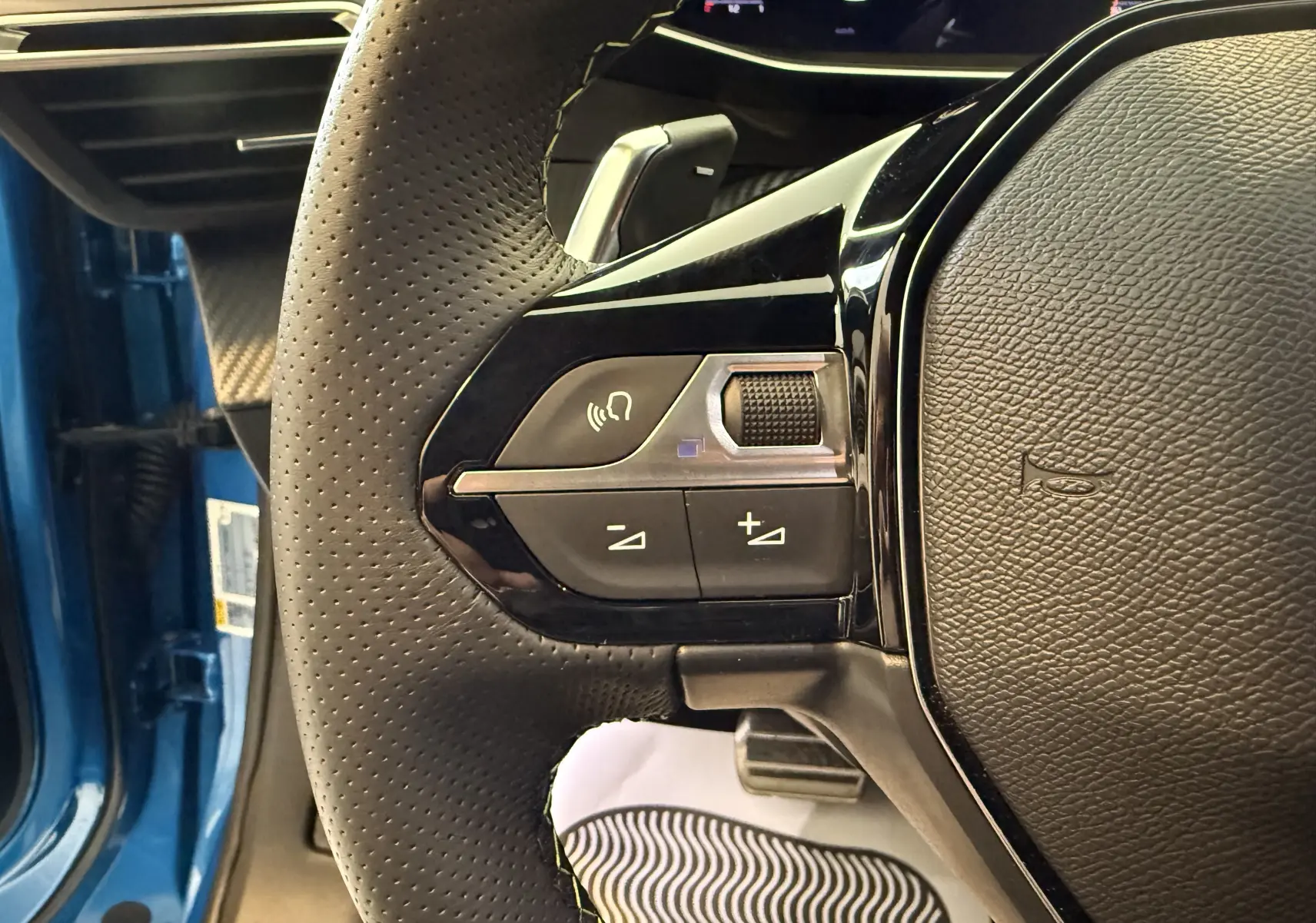 Gros plan sur le volant perforé côté gauche du Peugeot 2008 bleu Vertigo Metal avec commandes audio intégrées.