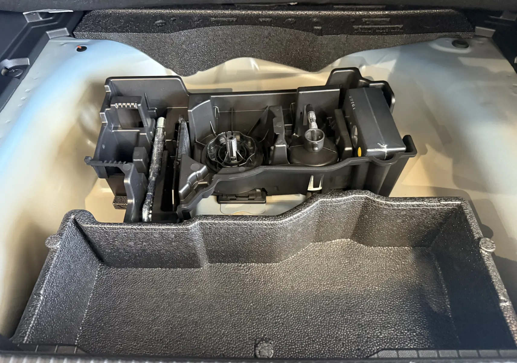 Vue rapprochée du rangement à outils dans le coffre d'un Peugeot 2008 2025 bleu Vertigo avec toit noir.
