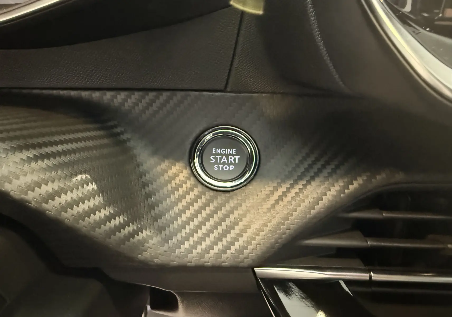 Gros plan sur le bouton start/stop entouré d'un habillage noir effet carbone dans l'habitacle du Peugeot 2008.
