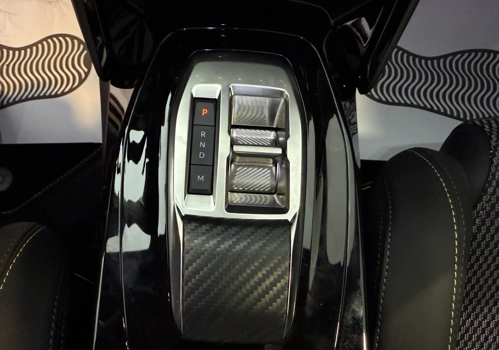 Vue plongeante sur la console centrale noire brillante du Peugeot 2008 GT 2025, avec sélecteur de boîte auto et finition carbone.