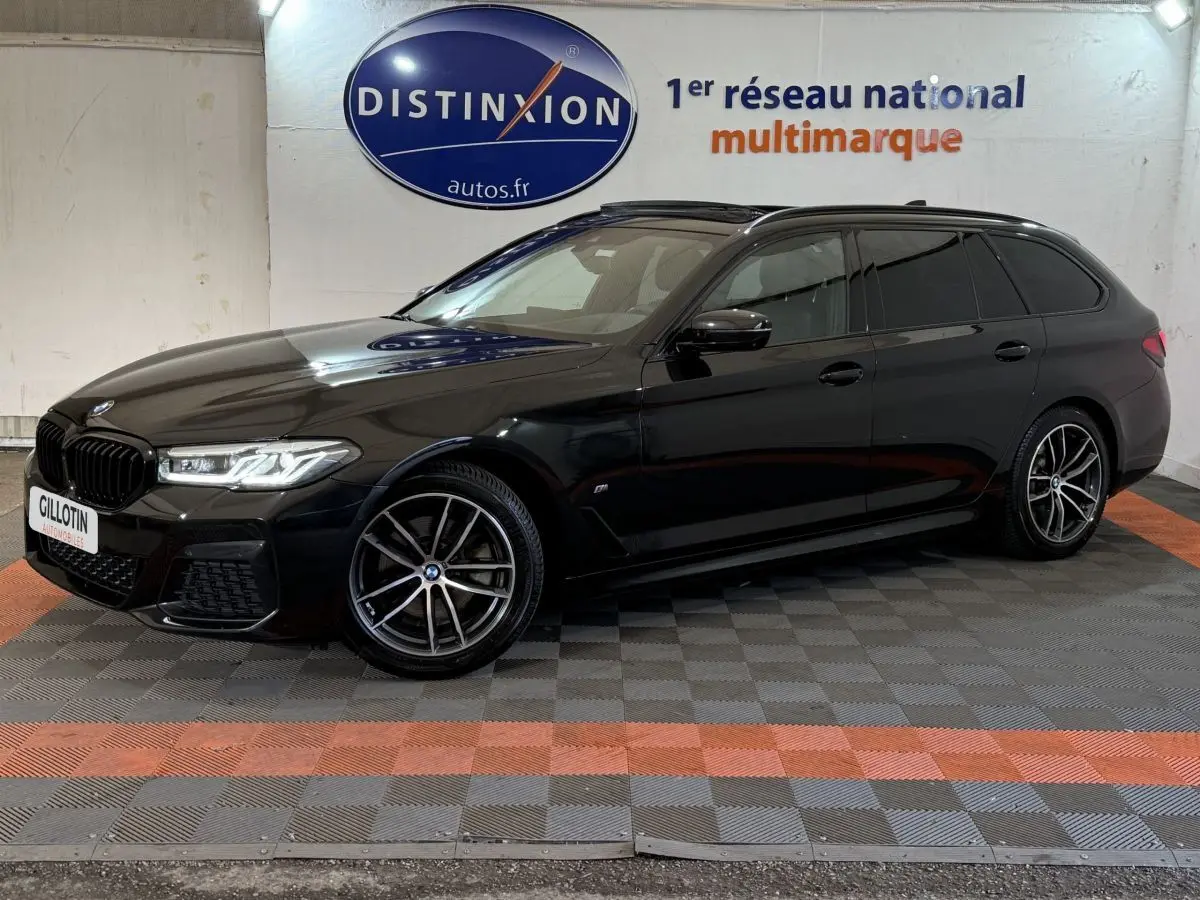 BMW Série 5 Touring 520d noir vue de profil droit en intérieur avec jantes M Sport et phares LED allumés.