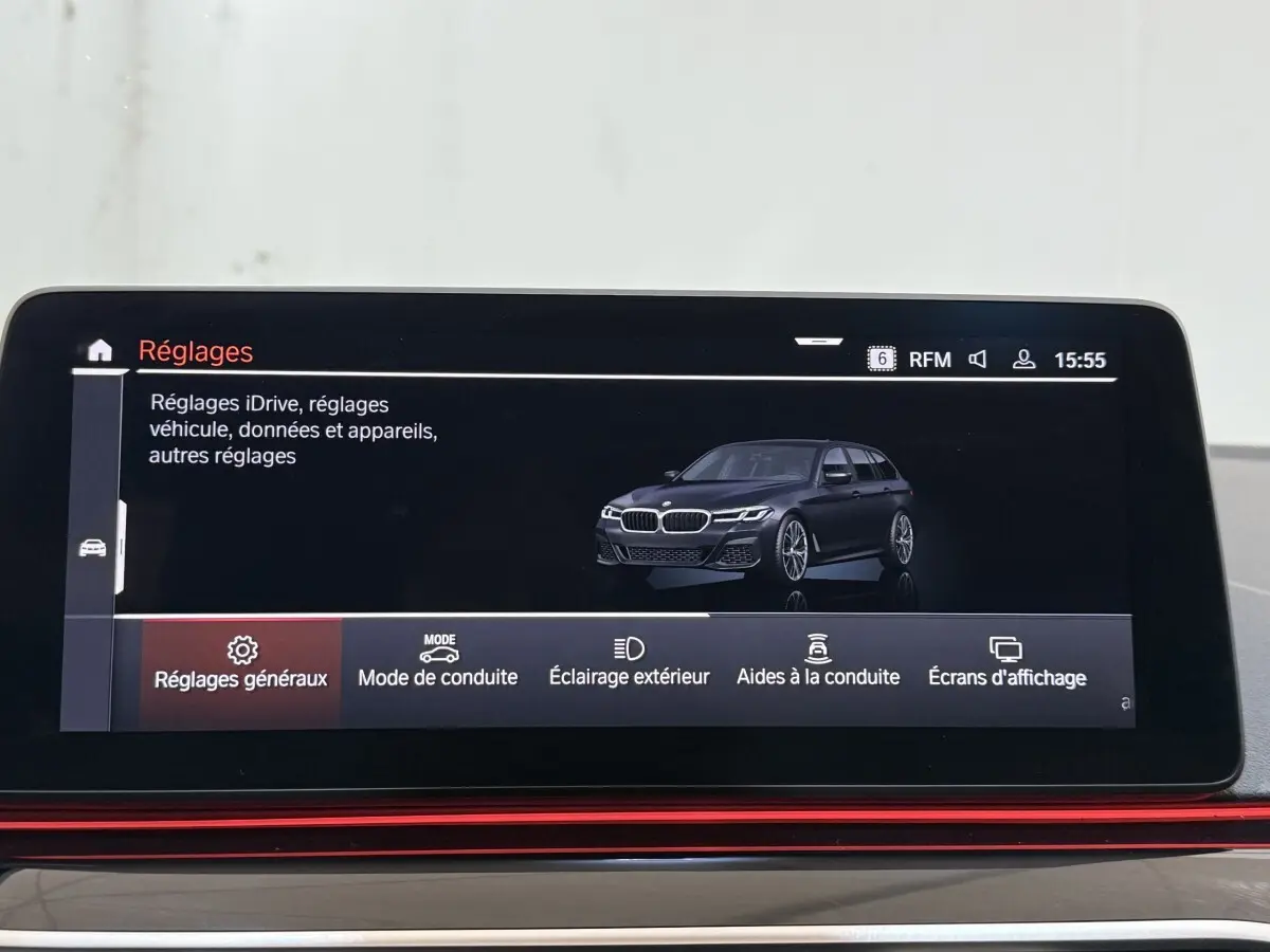 Écran tactile intérieur affichant une BMW Série 5 Touring noire en 3/4 avant dans le menu réglages.