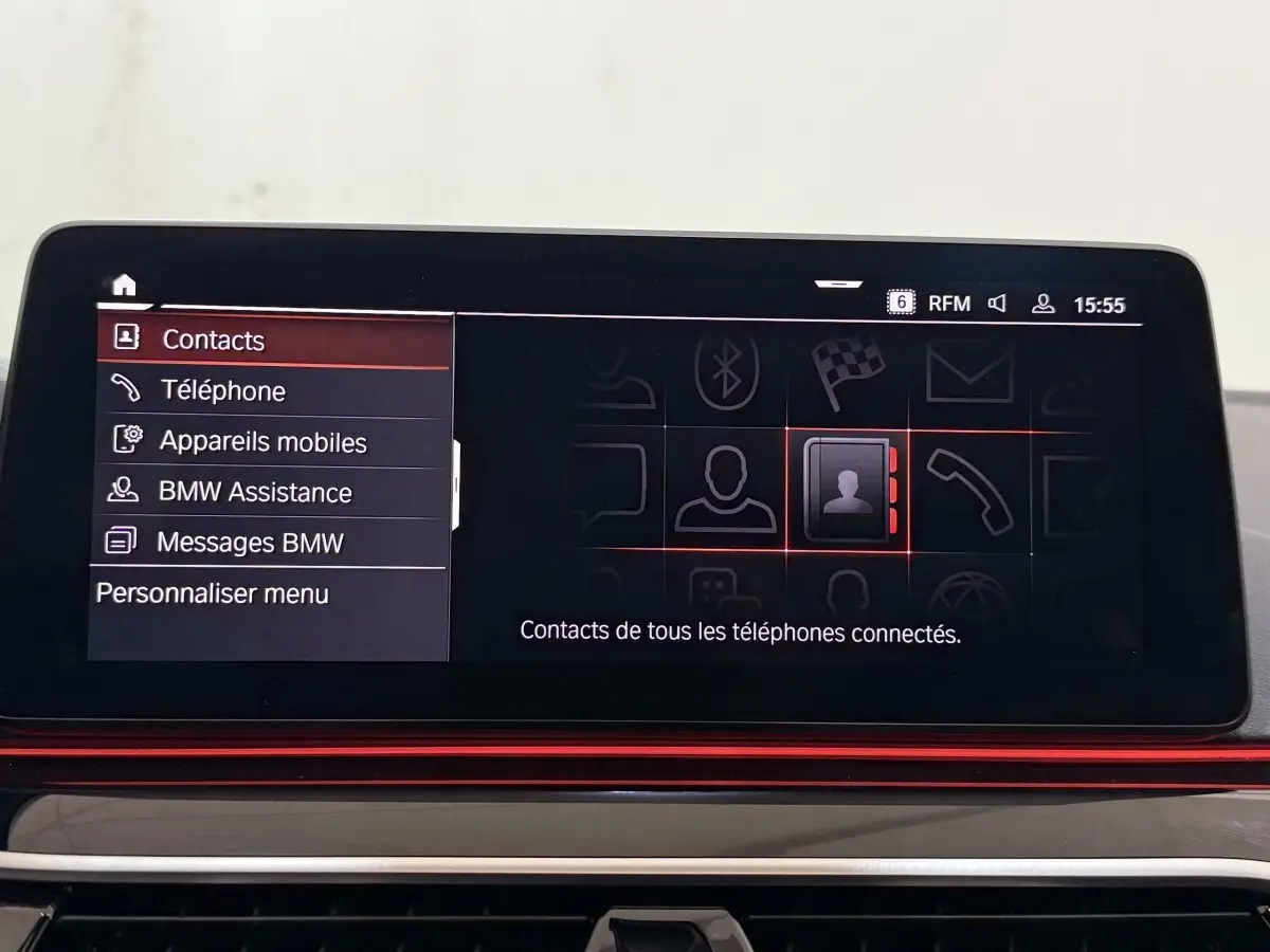 Écran tactile central de la BMW Série 5 Touring 520d M Sport 2023 affichant le menu contacts en intérieur noir et rouge.