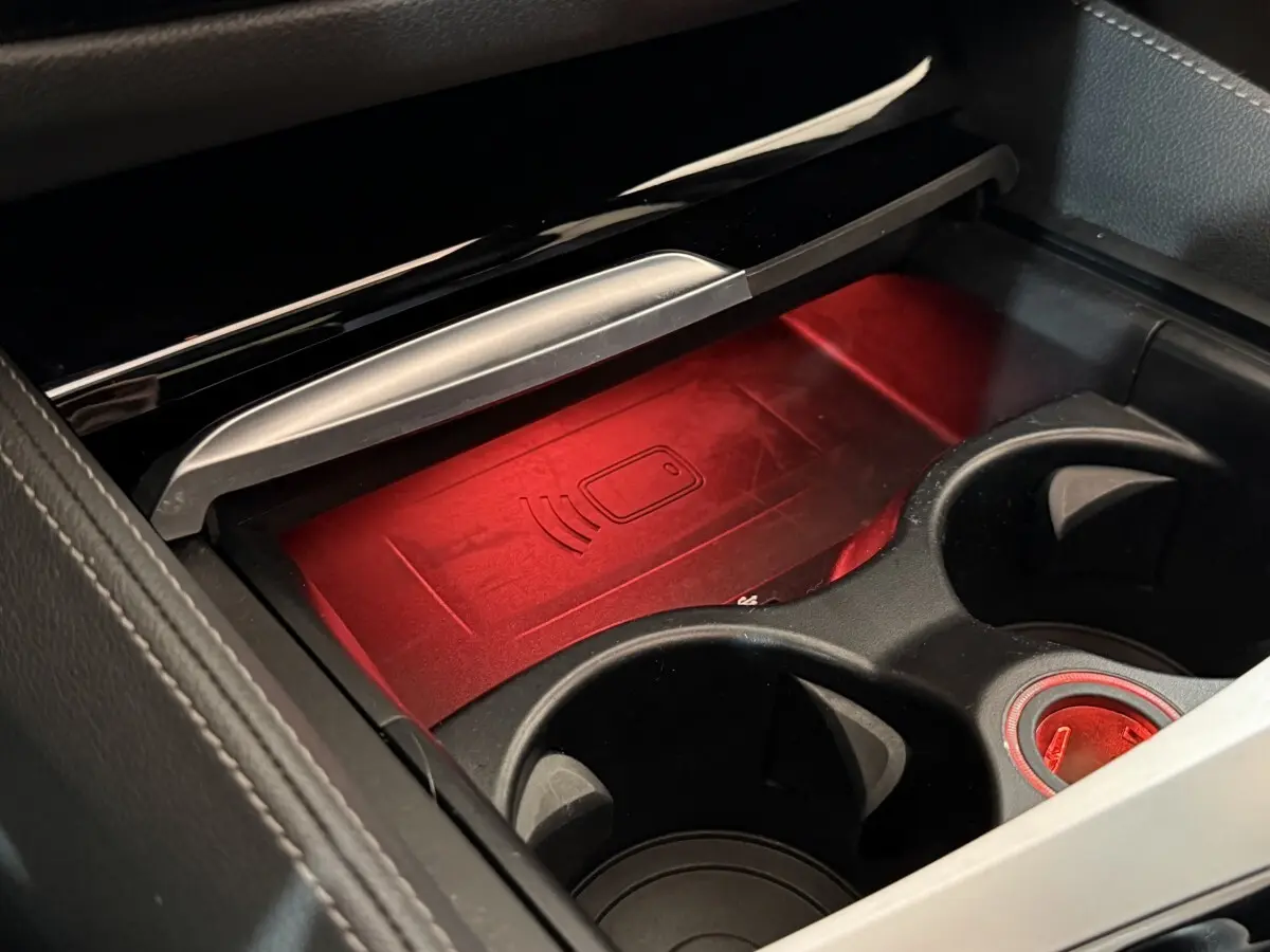Gros plan sur le compartiment central noir avec éclairage rouge et zone de recharge sans fil dans BMW Série 5 Touring 520d 2023.
