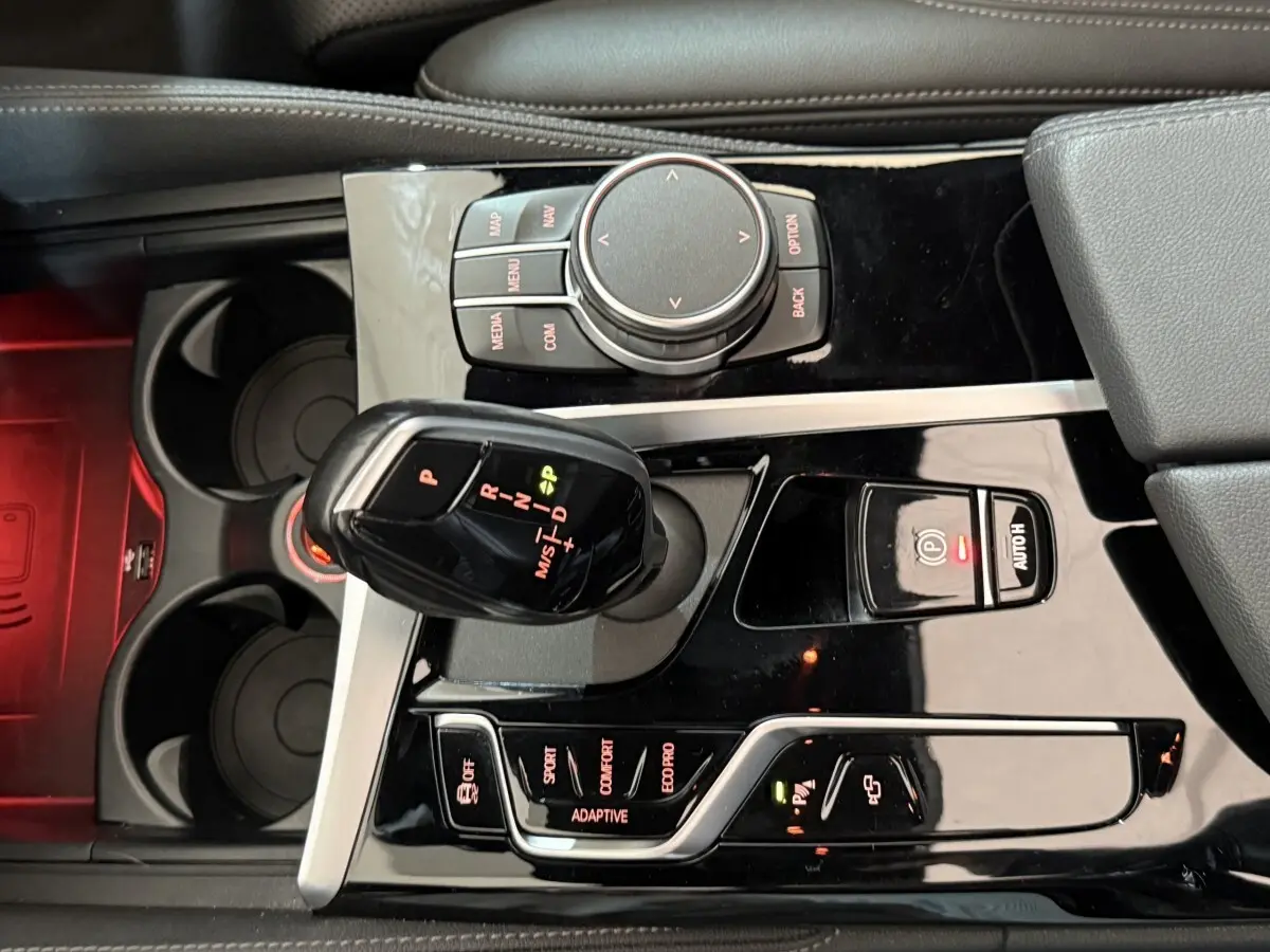 Vue rapprochée de la console centrale noire brillante de la BMW Série 5 Touring 520d avec levier de vitesses automatique et commandes.