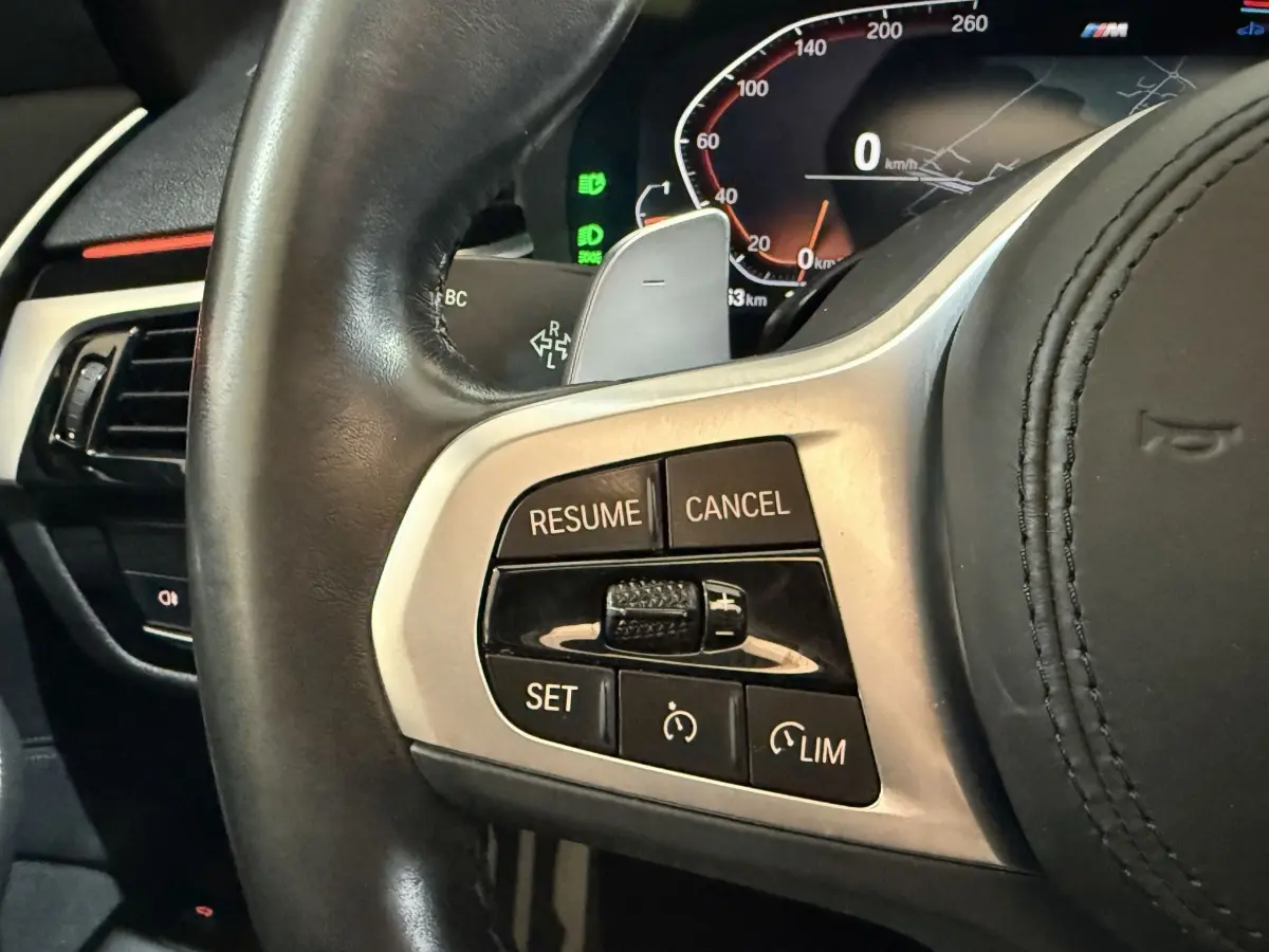 Gros plan sur le volant cuir noir de la BMW Série 5 Touring 520d M Sport 2023, avec commandes de régulateur de vitesse.