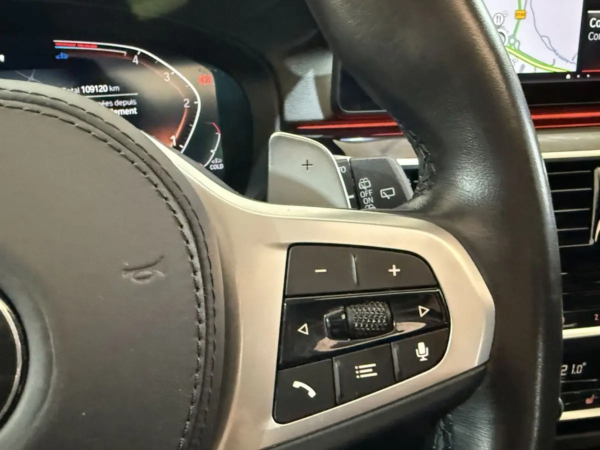 Gros plan sur le volant cuir noir de la BMW Série 5 Touring 520d, avec commandes multifonctions et écran digital en arrière-plan.