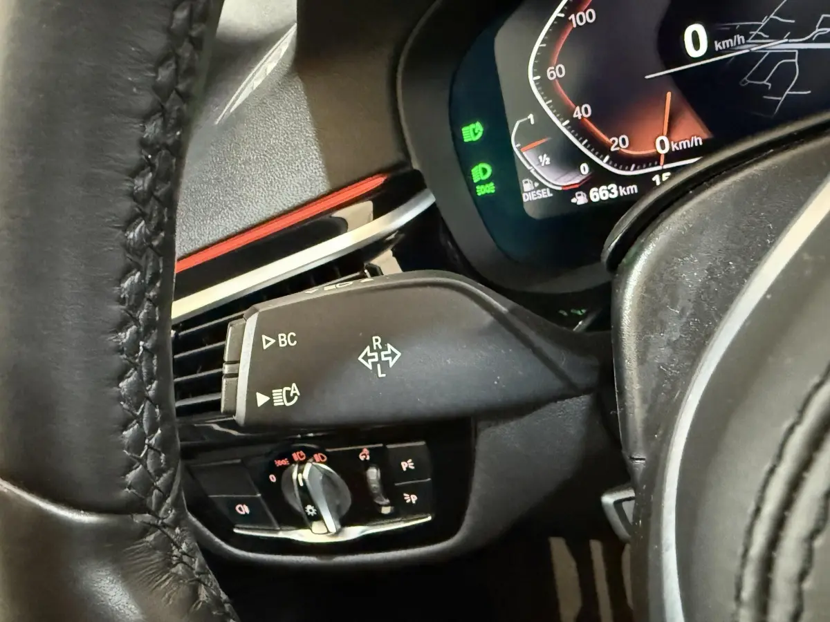 Gros plan sur la commande de clignotants et tableau de bord numérique d'une BMW Série 5 Touring noire, côté gauche du volant.