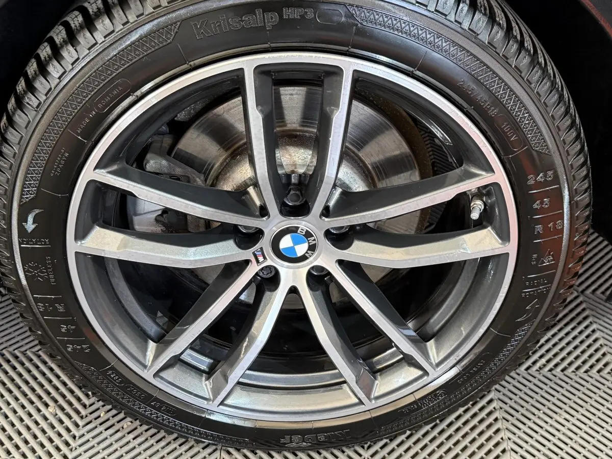 Gros plan sur la jante alliage bicolore et le pneu hiver d'une BMW Série 5 Touring noire.