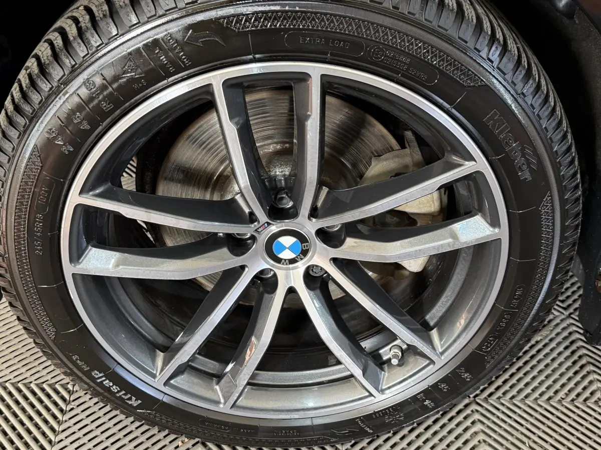Gros plan sur la jante alliage grise et noire avec logo BMW au centre, montée sur pneu Kleber.