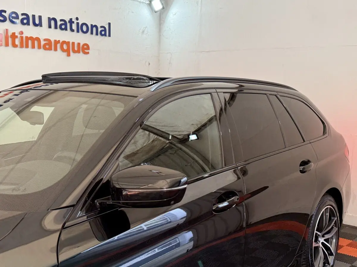 Vue de côté droit avant d'une BMW Série 5 Touring 520d noire avec vitres teintées et rétroviseur assorti.