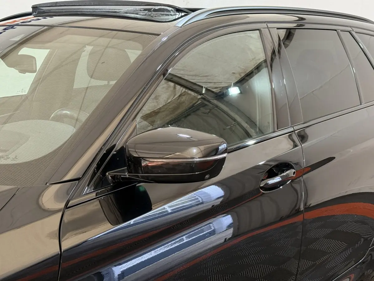 Gros plan sur la porte avant gauche noire d'une BMW Série 5 Touring 520d M Sport avec rétroviseur et poignée chromés.