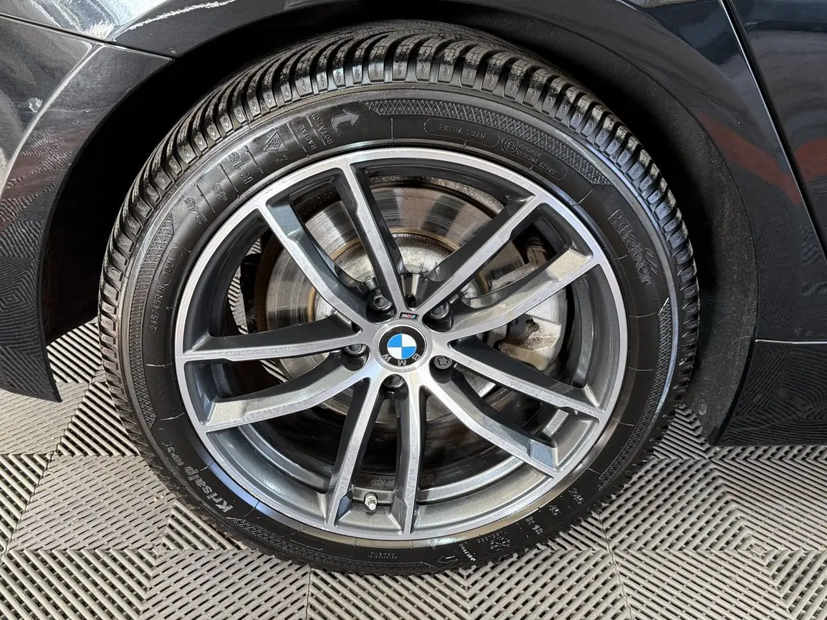 Gros plan sur la roue avant droite noire d'une BMW Série 5 Touring 520d M Sport avec jante alliage gris foncé.