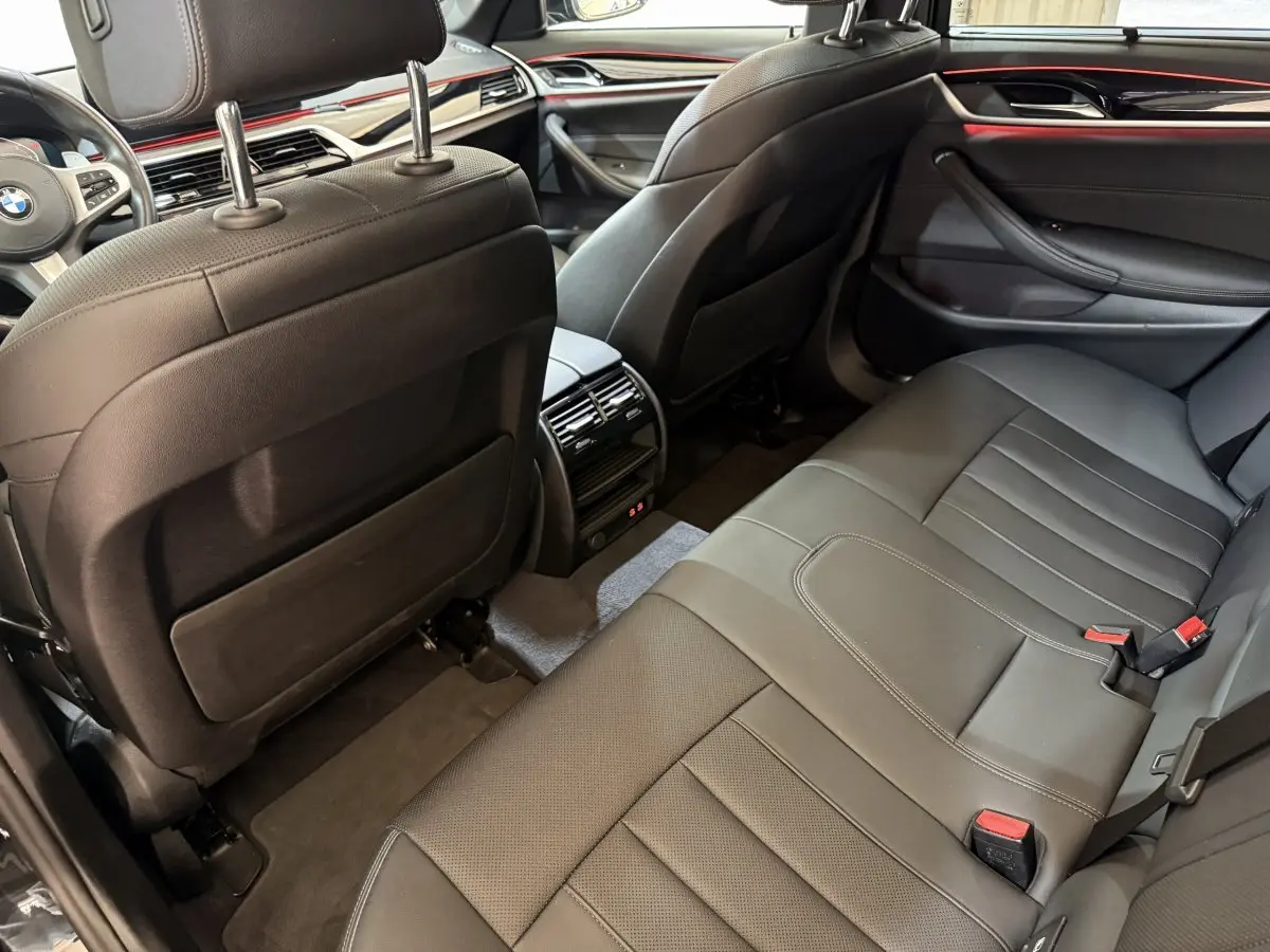 Vue intérieure arrière côté droit de la BMW Série 5 Touring 520d M Sport 2023 avec sièges cuir noirs et finitions rouges.