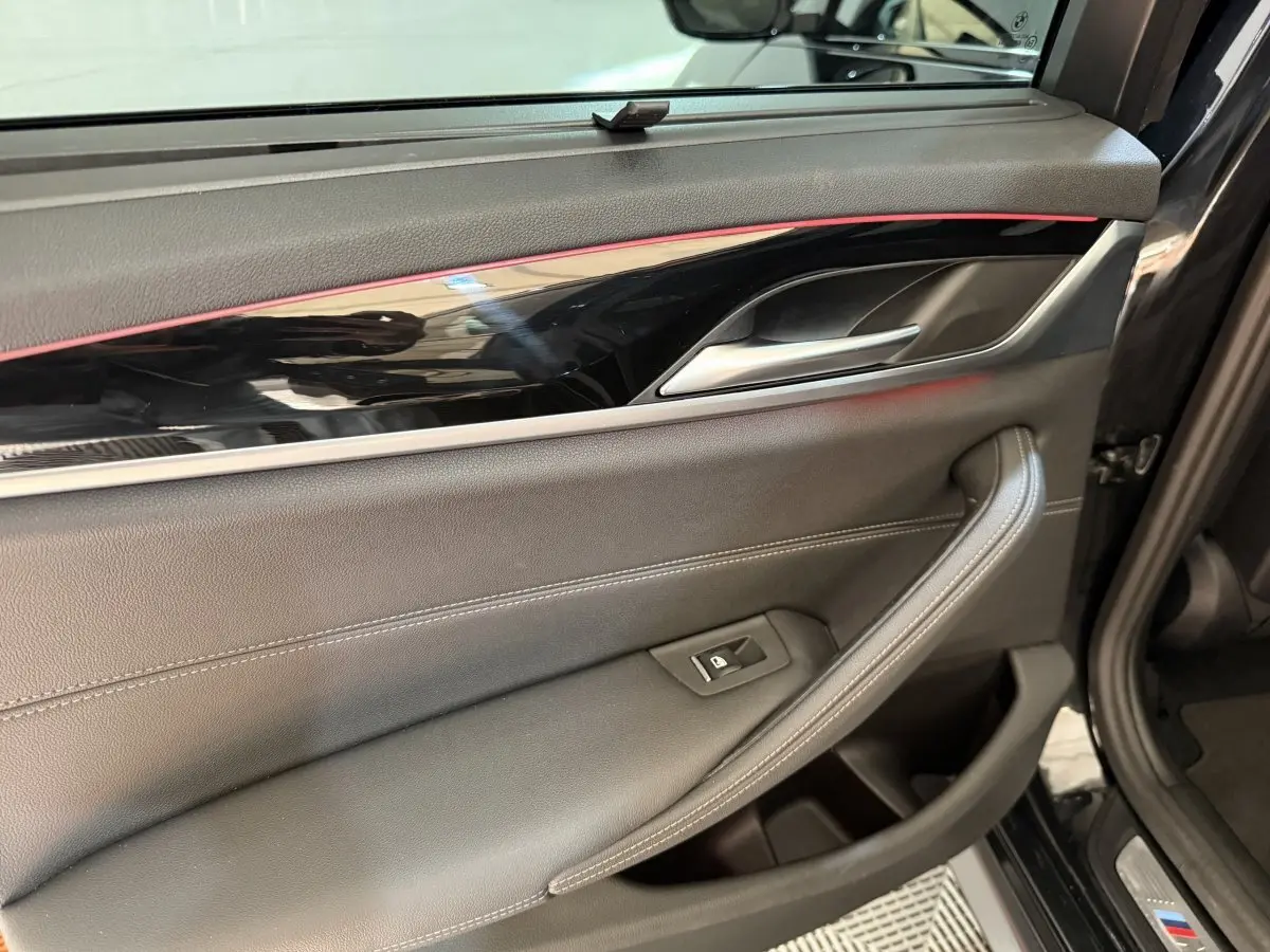 Détail de la porte intérieure côté gauche d'une BMW Série 5 Touring noire avec insert brillant et éclairage d'ambiance rouge.
